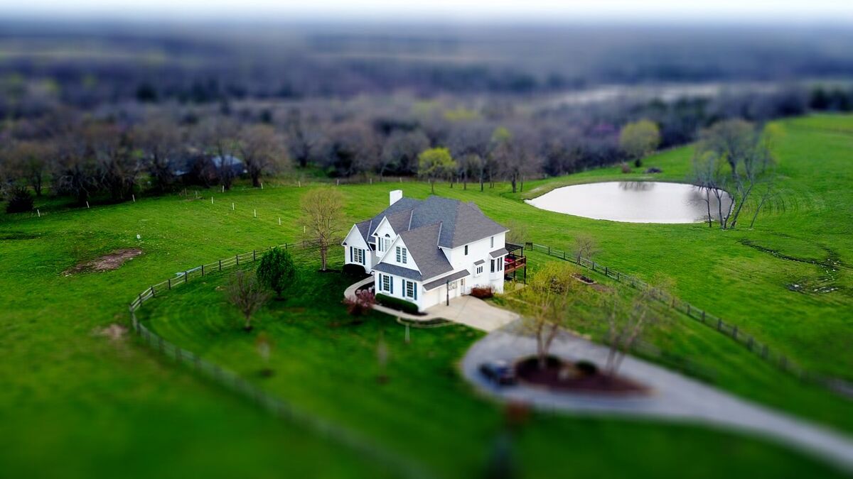 Aerial view of a country home on rolling acreage with a long curving driveway through green pasture