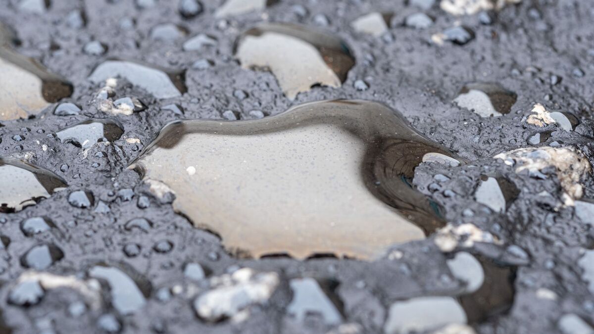 A rain-filled pothole broken through a worn asphalt surface, with loose aggregate around its edges