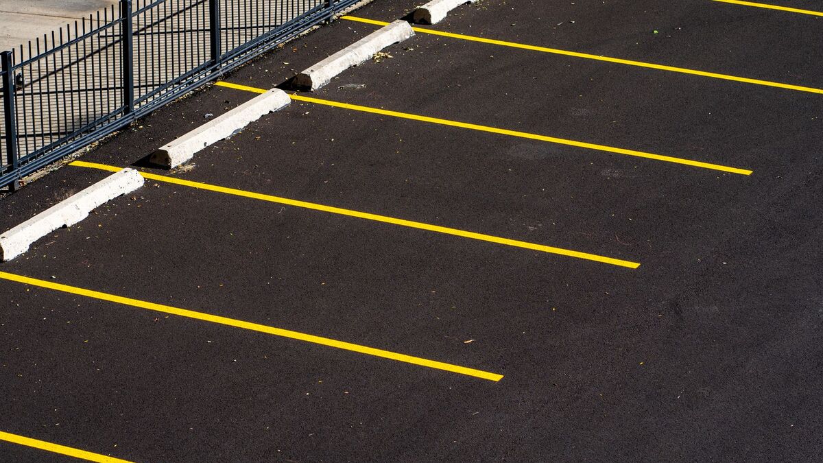 A freshly paved black parking lot with bright yellow stall lines and concrete wheel stops