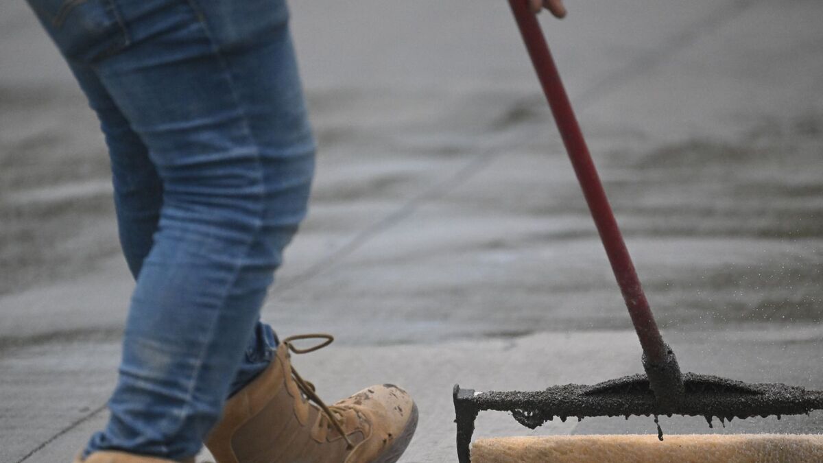 A worker spreading a fresh coat of black sealer across asphalt with a long-handled squeegee
